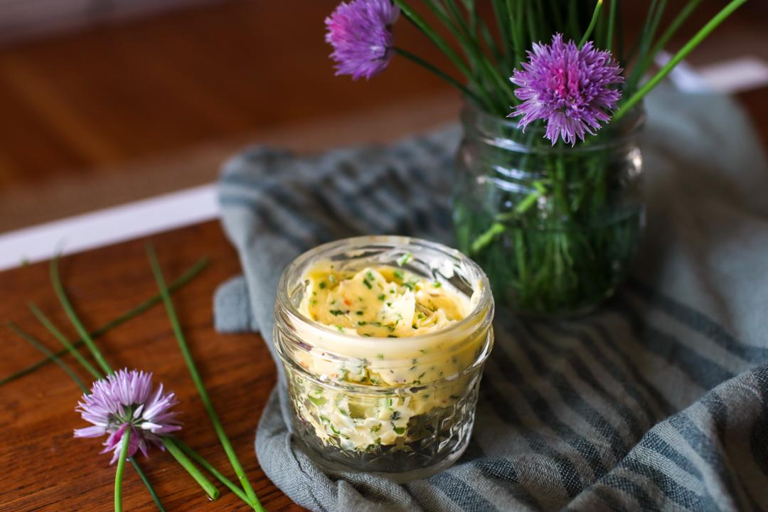 finished chive butter in a jar with chive flowers around it
