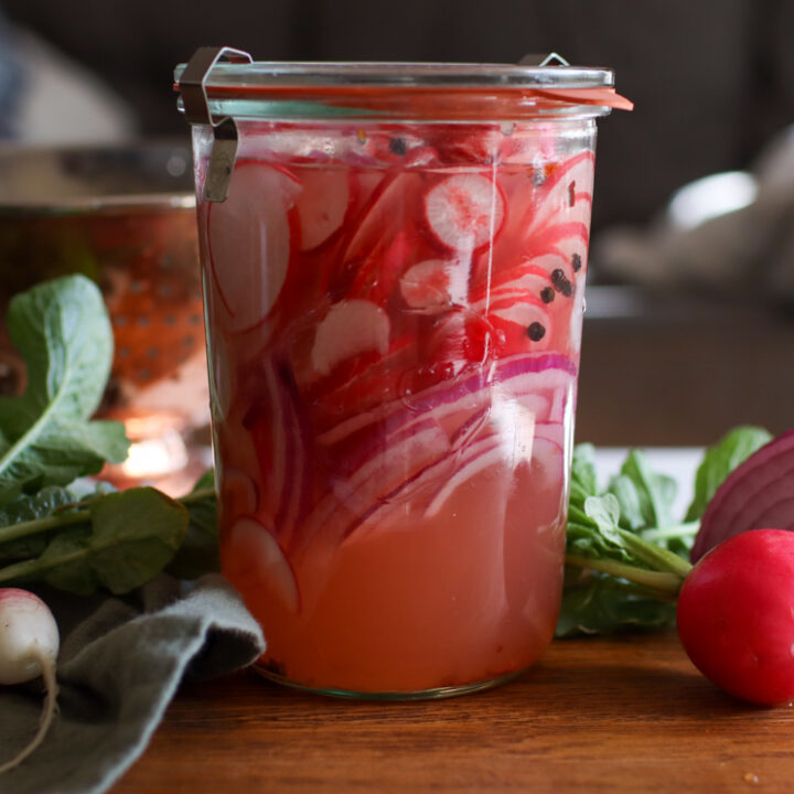 jar of pickled radishes on a counter with radishes around it