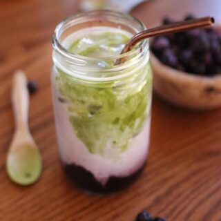 a blueberry matcha latte with a spoon of matcha and a bowl of blueberries.