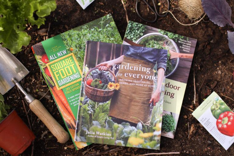 A photo of three vegetable gardening books with a shovel, plants, and seeds around it.