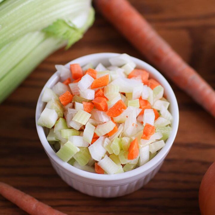 A bowl of mirepoix with celery, carrots, and an onion around it.