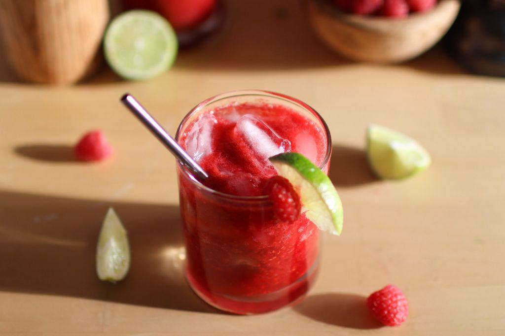 Looking down on a raspberry margarita with raspberries and limes on the table around it.