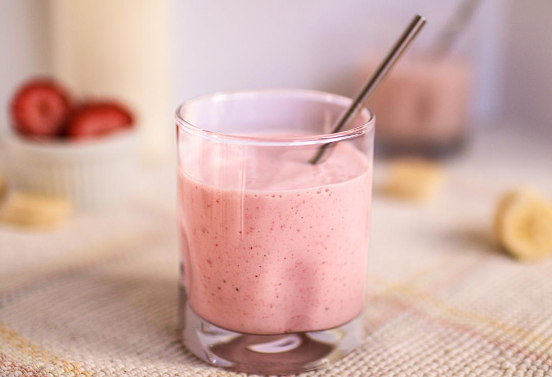 A photo of a strawberry banana smoothie with strawberries, milk, bananas and a second smoothie in the background.
