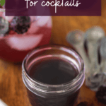 a jar of blackberry syrup with a cocktail in the background