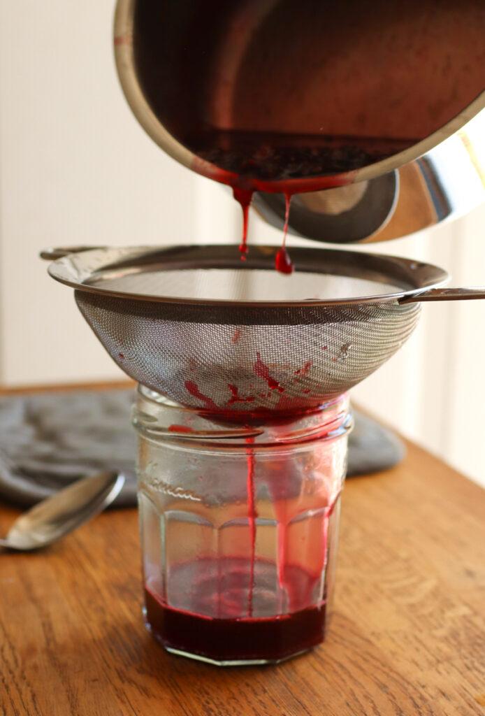 pouring blackberry syrup through a fine mesh strainer into a glass jar