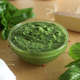 a bowl of nut-free pesto with basil, cheese, and garlic around it