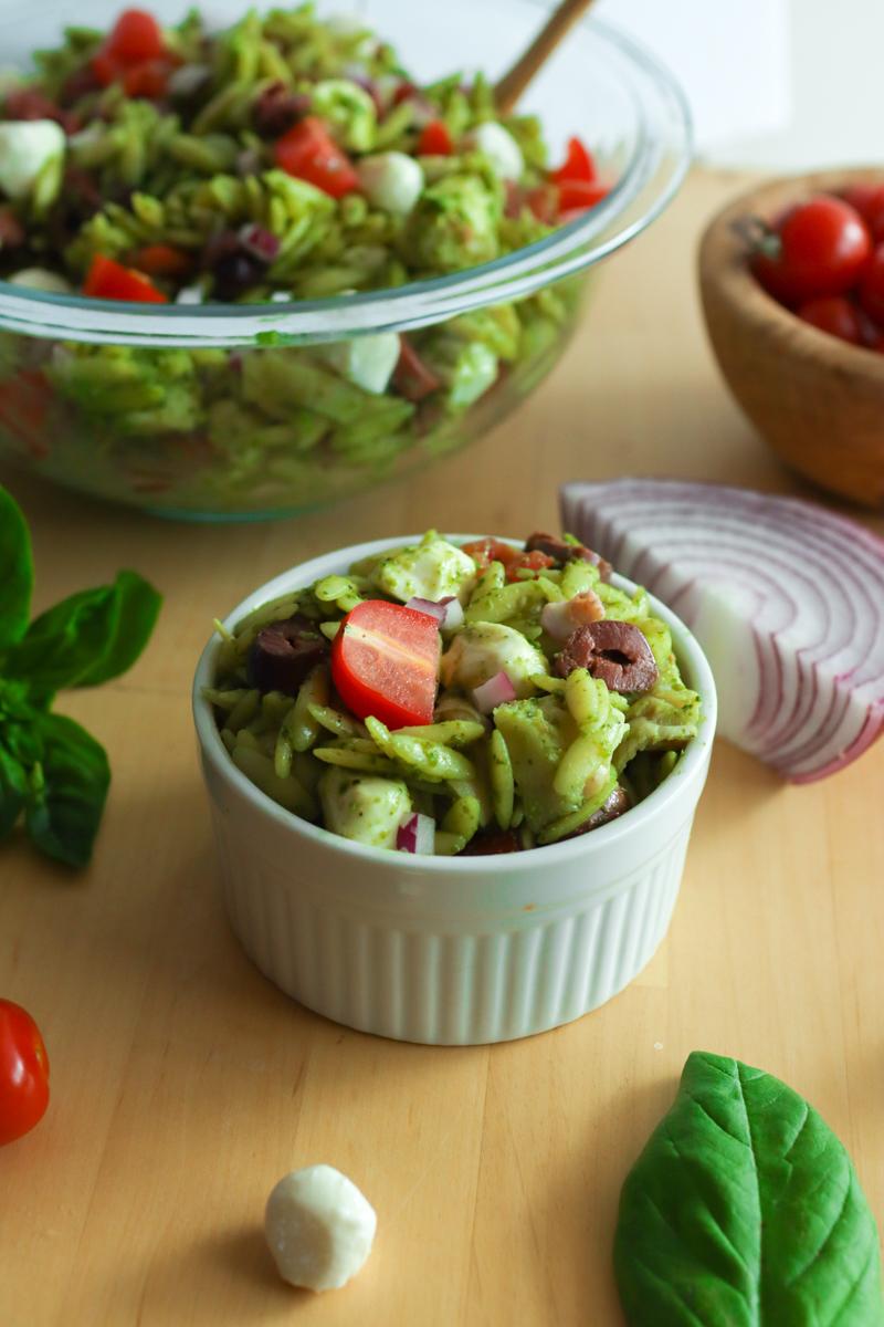 a bowl of pesto orzo pasta salad with an onion, mozzarella, and basil.