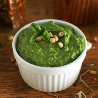 a bowl of pesto sitting on a counter with cheese, garlic, and basil