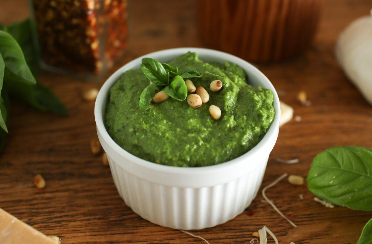 a bowl of pesto sitting on a counter with cheese, garlic, and basil