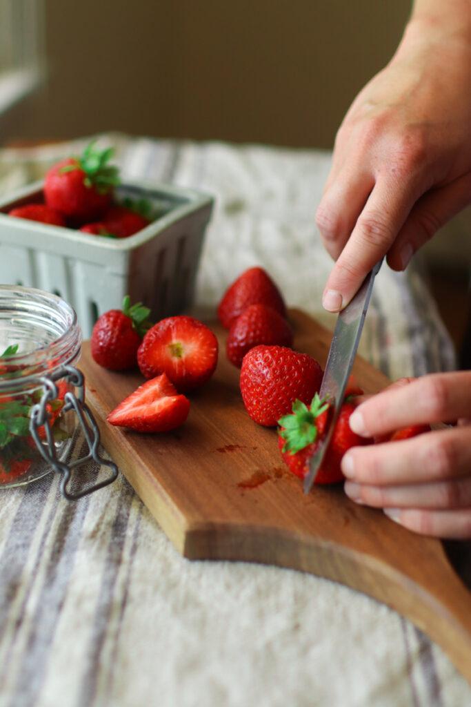 a hand cutting strawberries on a wooden cutting board