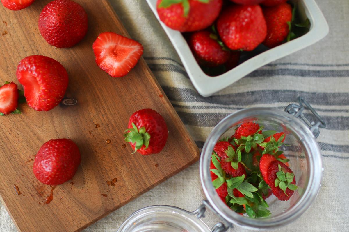 looking down on a jar of strawberry tops and a cutting board with fresh strawberries