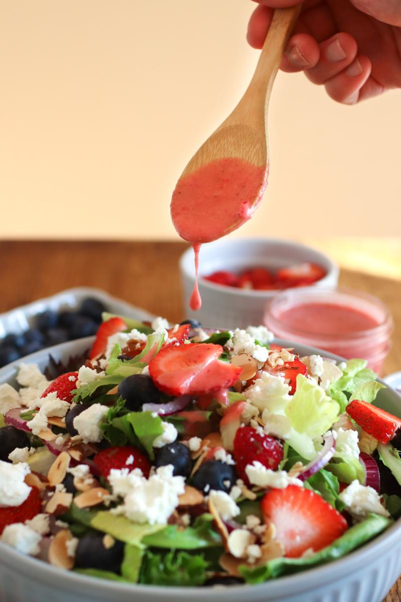 A spoon drizzling strawberry vinaigrette onto a summer berry salad