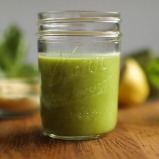 A jar of basil dressing with parmesan, lemon, and basil behind it