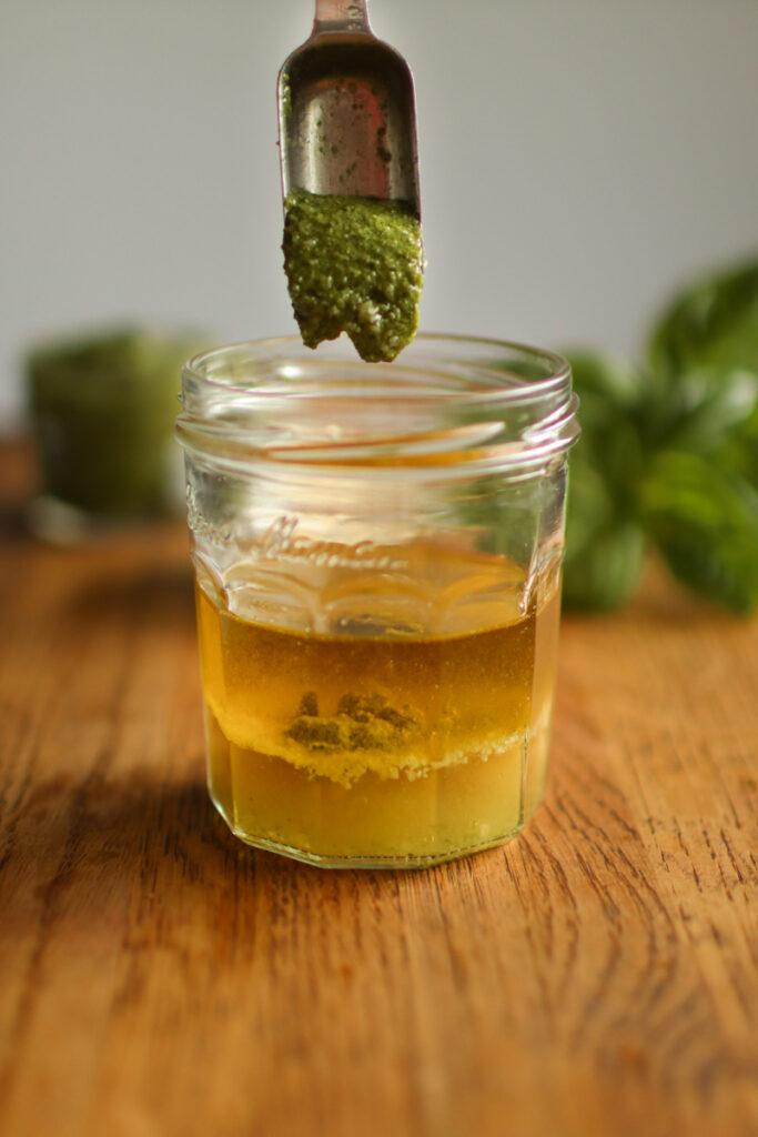 pesto being dropped into a jar of dressing ingredients