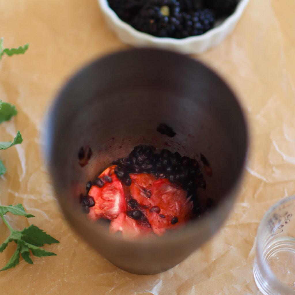 lemons and blackberries in a cocktail shaker after being muddled