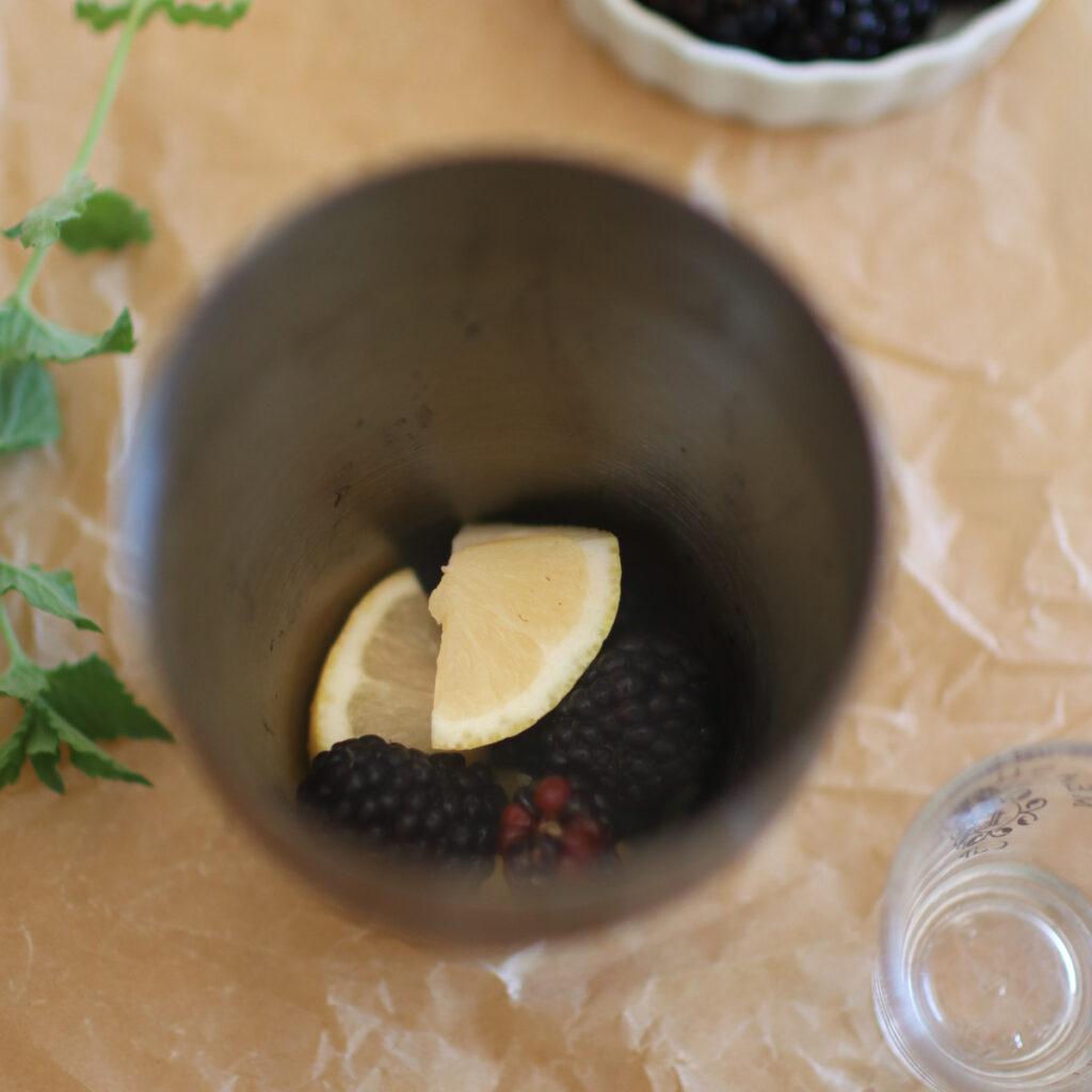 lemons and blackberries in a cocktail shaker before being muddled