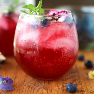 a glass of blueberry gin fizz with blueberries and a second cocktail in the background