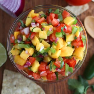 Looking down on a bowl of mango pico de gallo with chips, lime, and a jalapeno