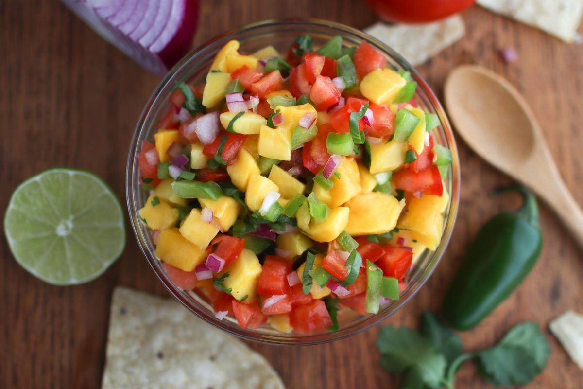 Looking down on a bowl of mango pico de gallo with chips, lime, and a jalapeno