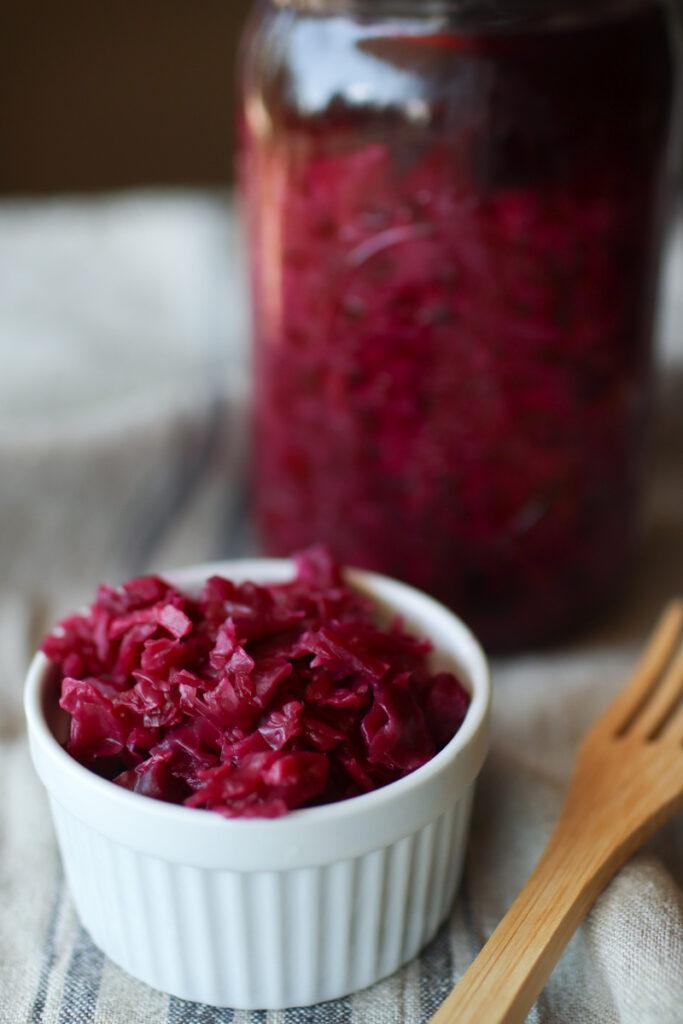 a bowl of fermented red cabbage, a fork, and a jar of cabbage