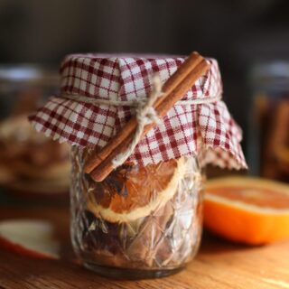 a simmer pot jar with a red plaid fabric topper and a cinnamon stick tied to it