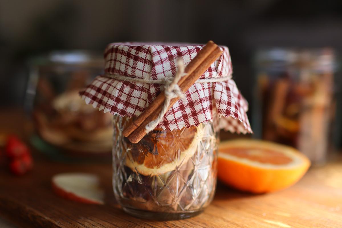 a simmer pot jar with a red plaid fabric topper and a cinnamon stick tied to it