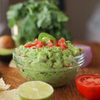 A bowl of guacamole with a tomato and lime