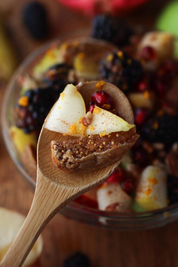 a spoon holding a scoop of fruit salad over a bowl of fruit salad