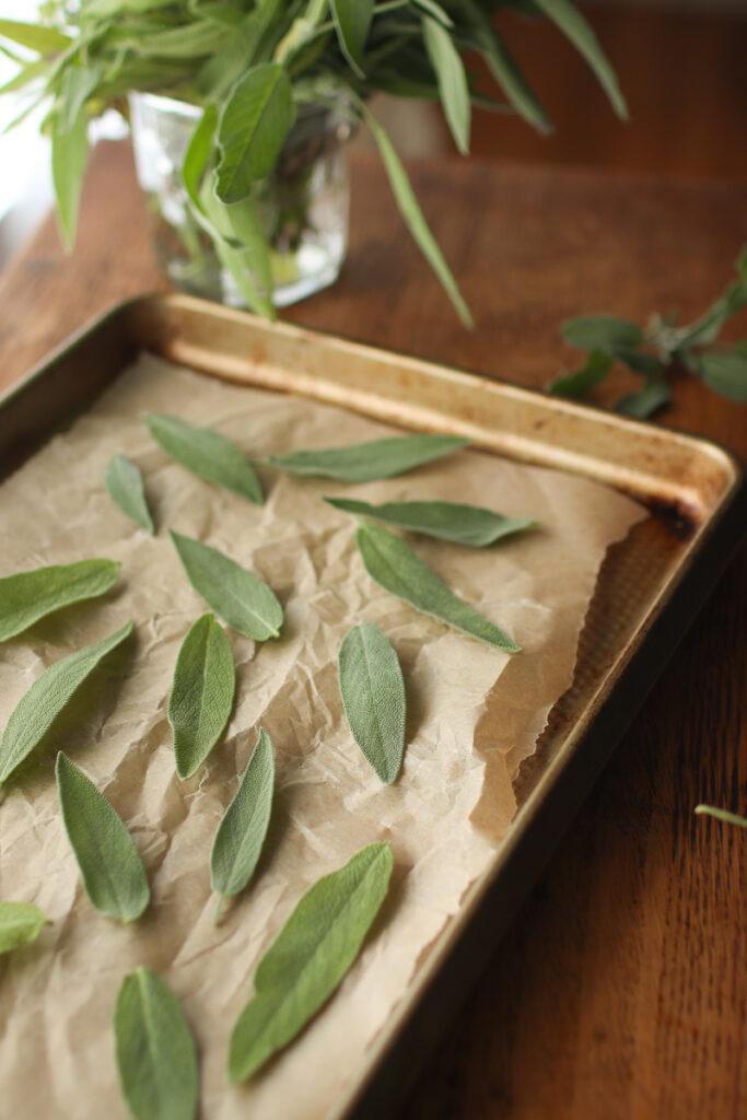 a baking tray with sage leaves laying on it. A jar of sage in the background.