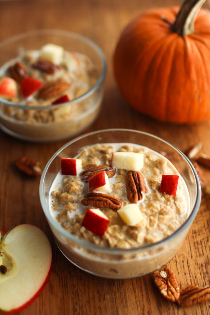 two bowls of pumpkin oatmeal with a pumpkin and an apple half