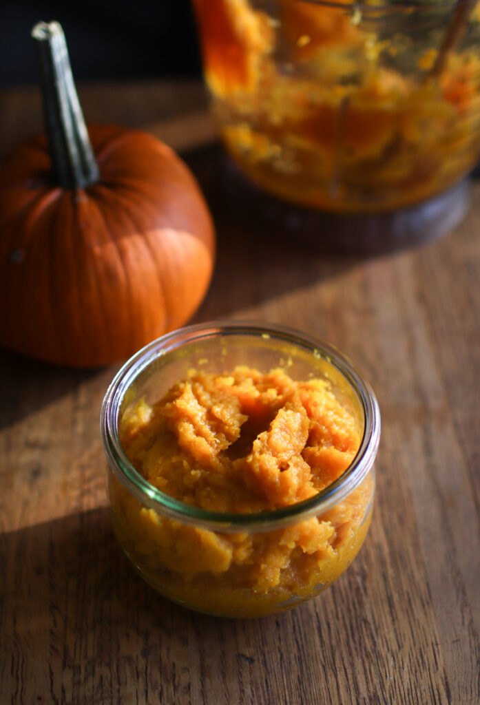 a jar of pumpkin puree with a pumpkin and a food processor in the backgroud