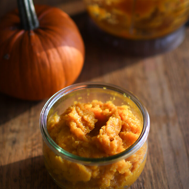 a jar of pumpkin puree with a pumpkin and a food processor in the backgroud