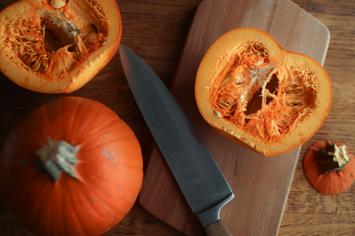 looking down on a cutting board with a cut pumpkin, whole pumpkin and a knife