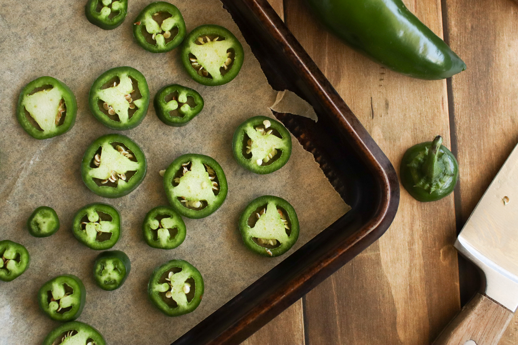 Sliced jalapeno peppers on a baking sheet.