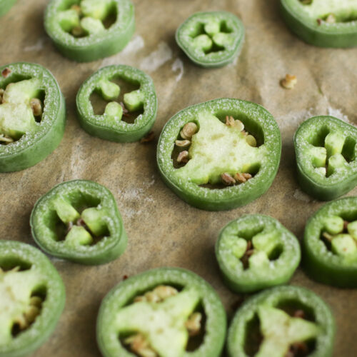 Frozen jalapeno slices on a piece of parchment paper.
