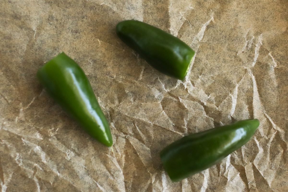 Three whole peppers on a piece of parchment paper.