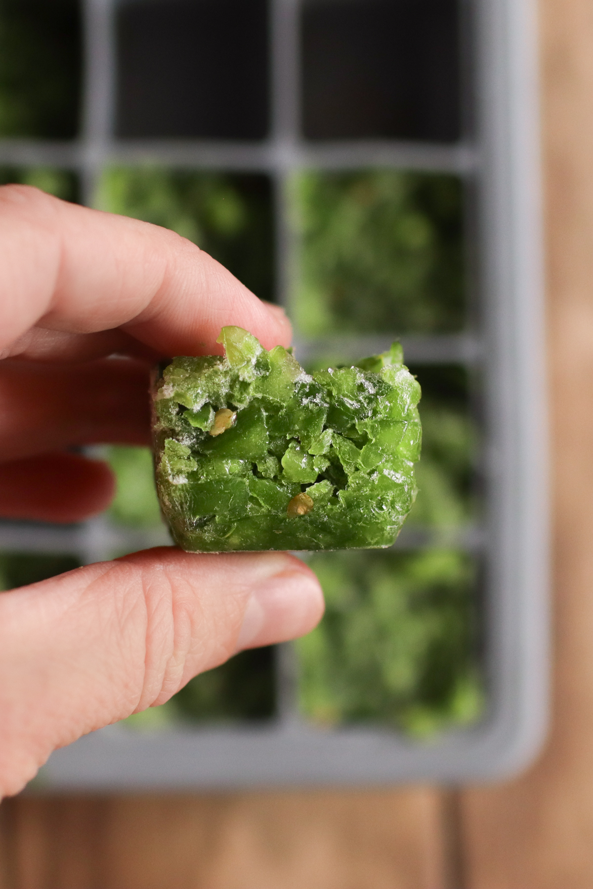A frozen jalapeno cube being held up over an ice cube tray.