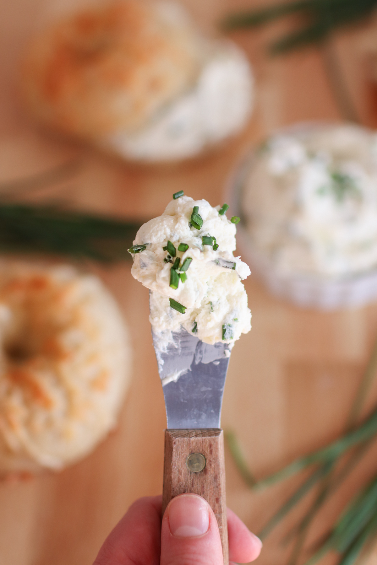 Holding a spreader with chive and onion cream cheese on it.