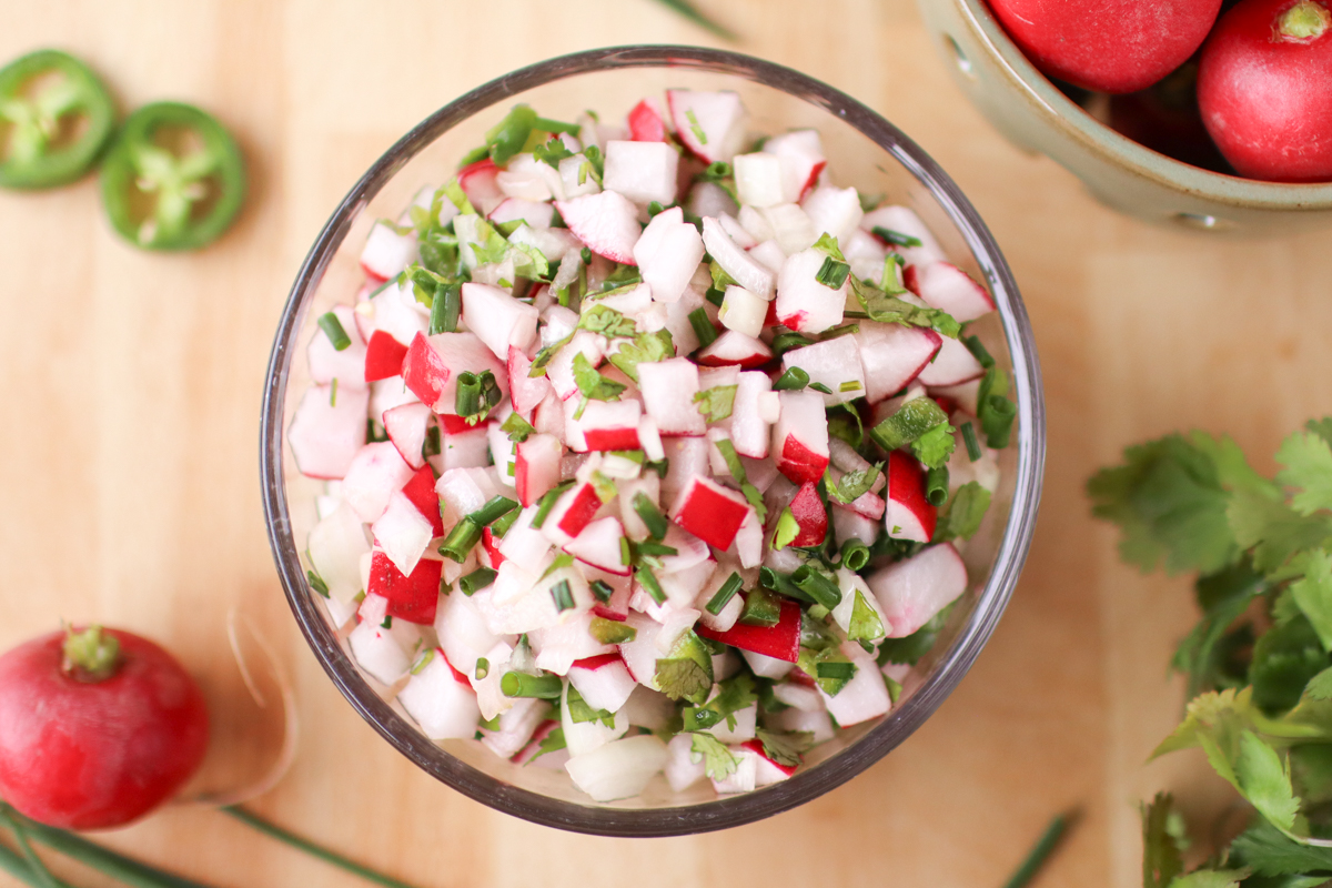 A bowl of radish salsa surrounded by radishes, jalapeno slices, and cilantro.