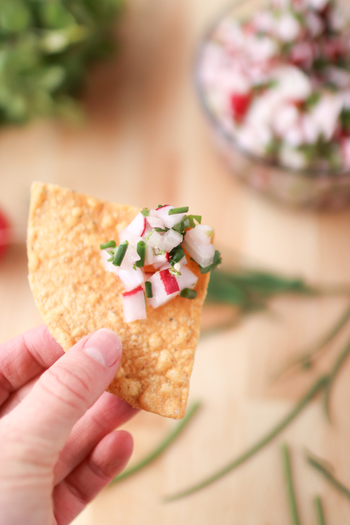 Holding a tortilla chip with a scoop of radish salsa on it.