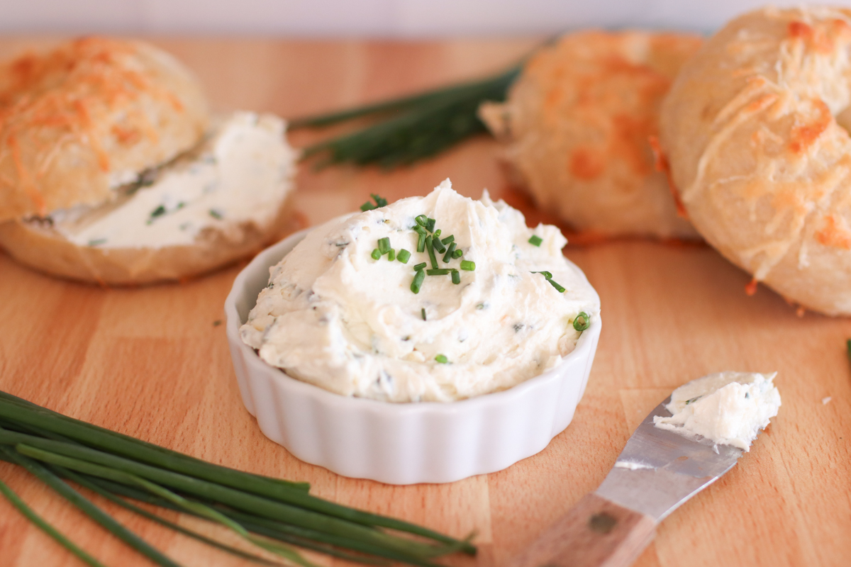 A bowl of chive and onion cream cheese with bagels and fresh chives.