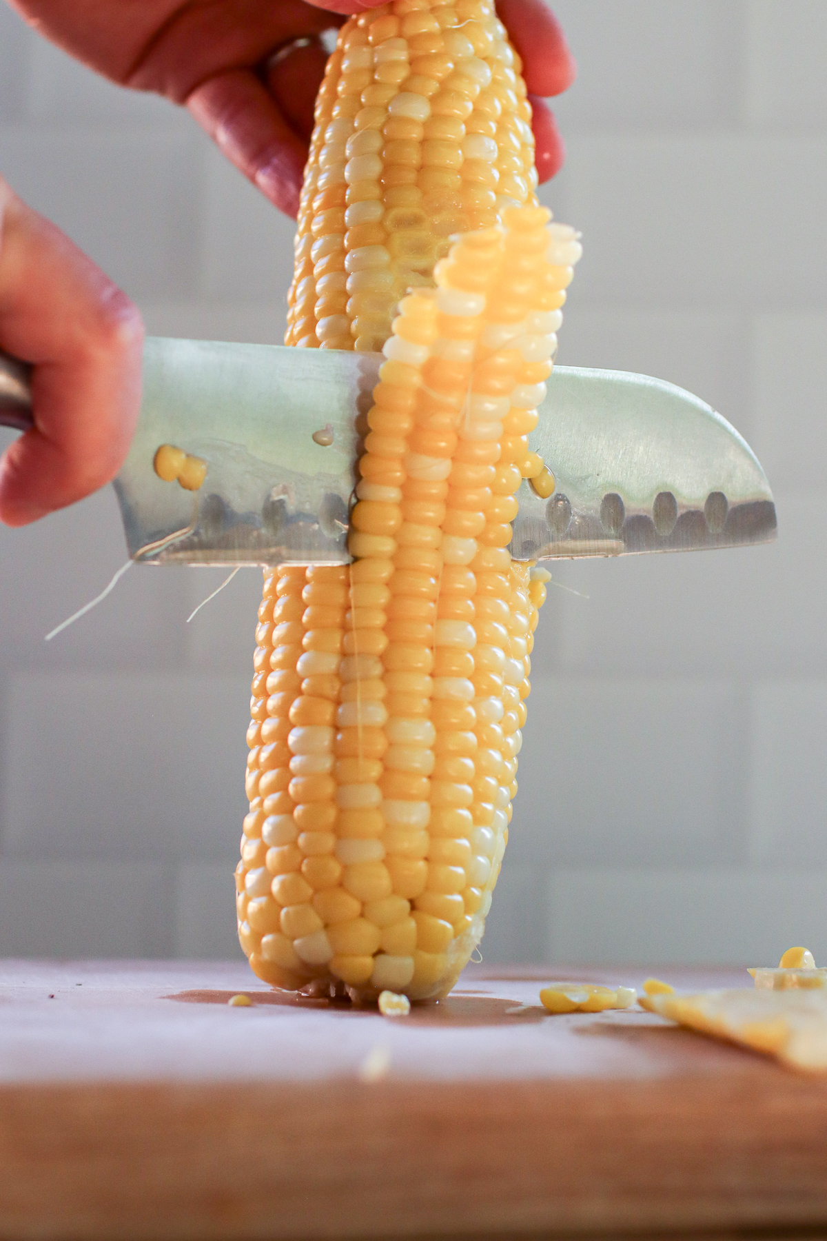 Cutting blanched corn off the cob on a wooden cutting board.