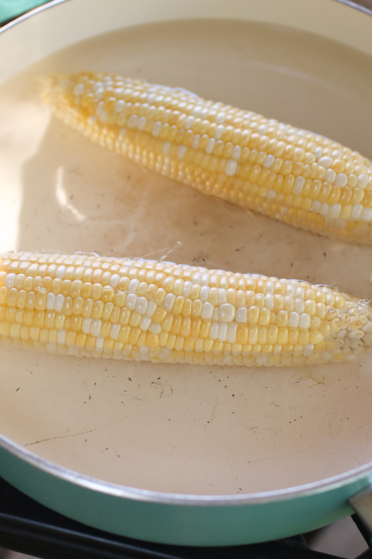 Boiling corn on the cob in a teal pot.