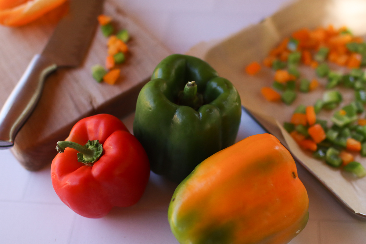 Bell peppers, a knife and cutting board, and a baking sheet lined with parchment paper. 