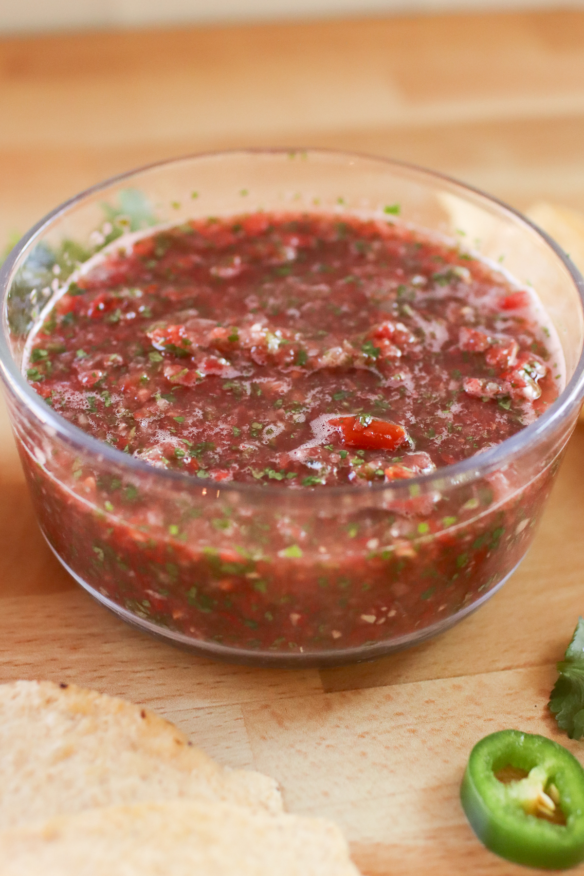 A bowl of blender salsa with chips and jalapenos next to it. 