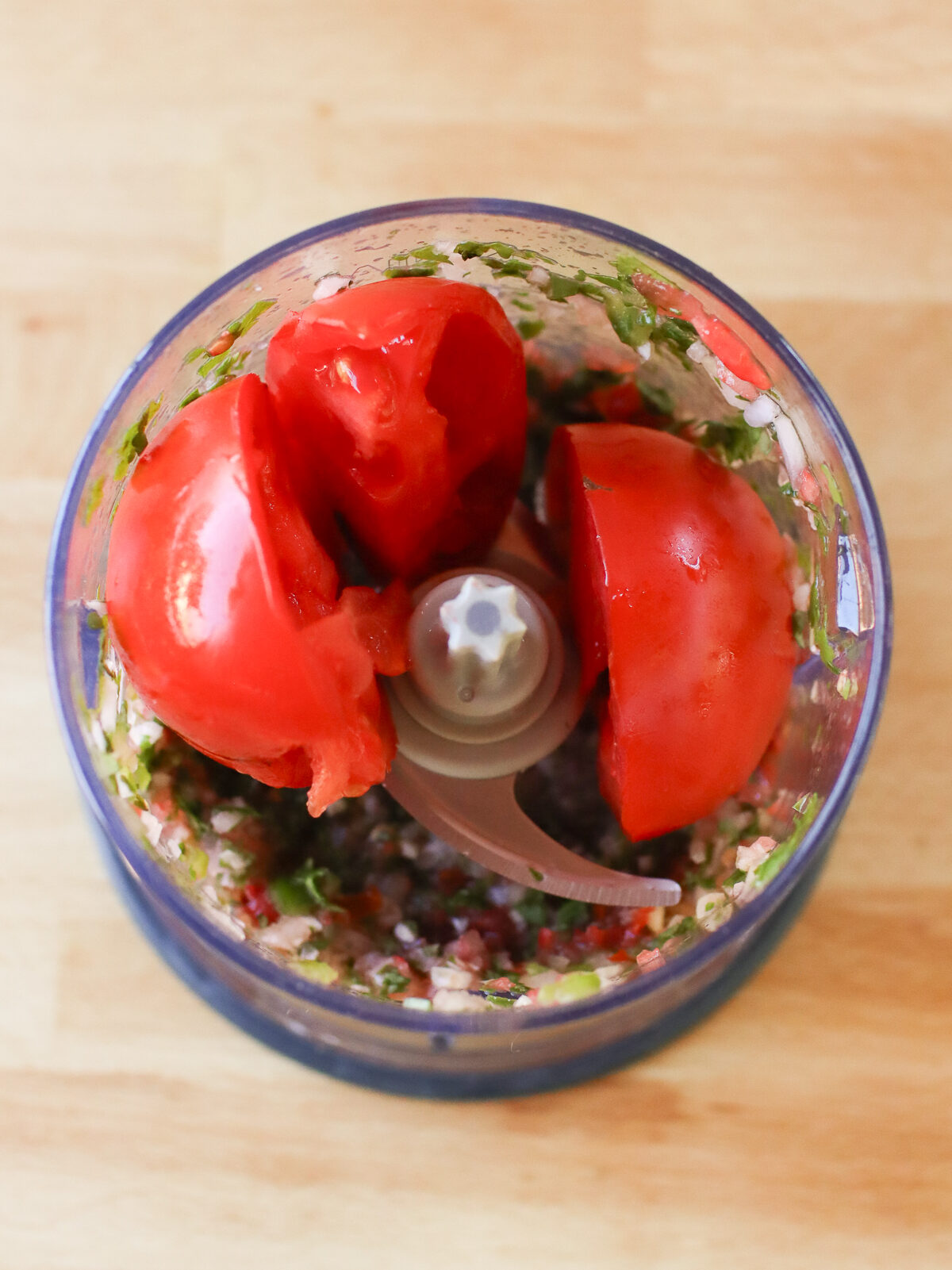 Adding more tomatoes to the small food processor. 