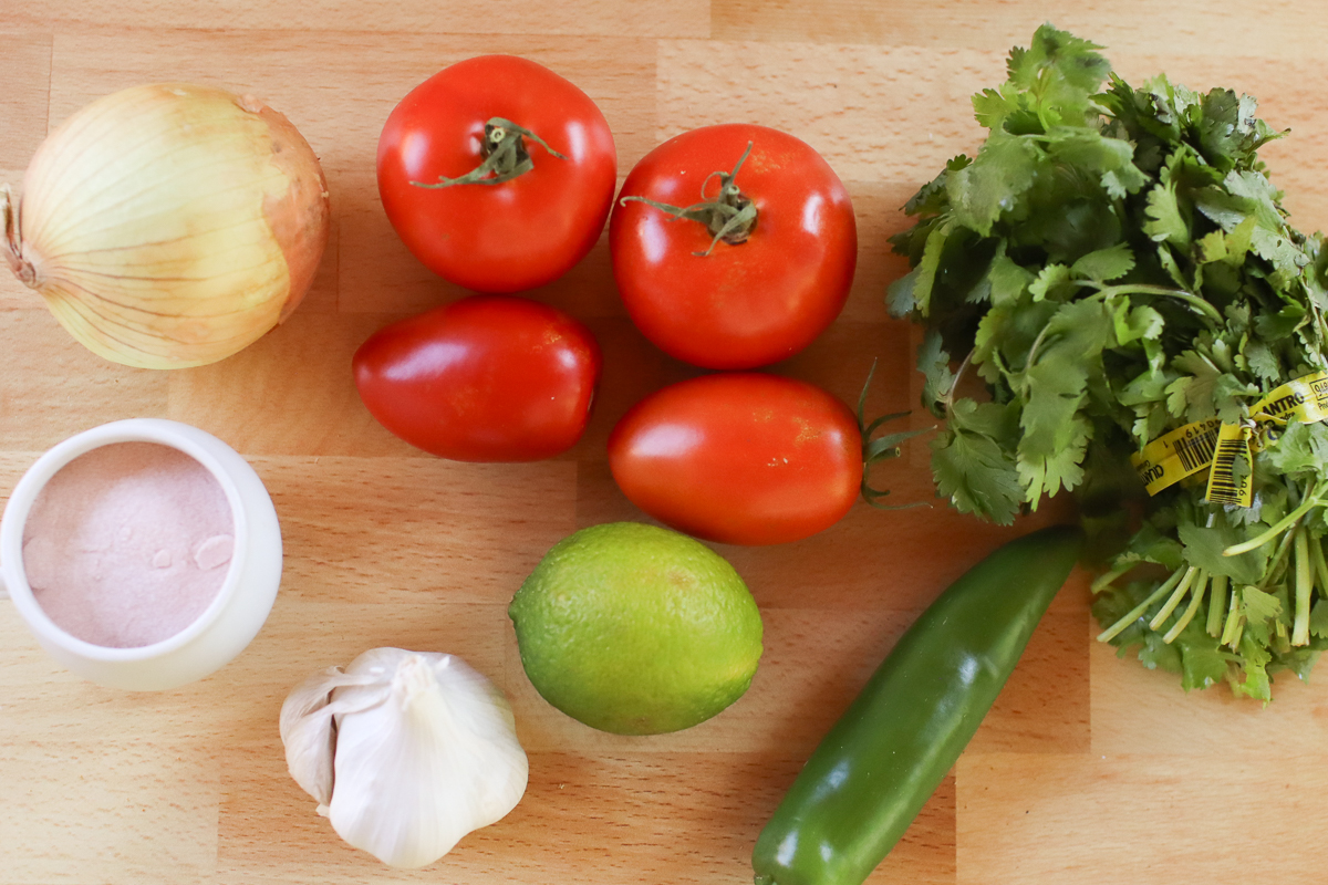 Fresh tomato blender salsa ingredients on a wooden table.