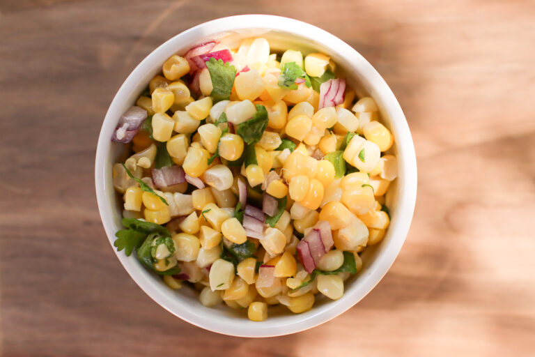 A bowl of corn salsa on a wooden table.
