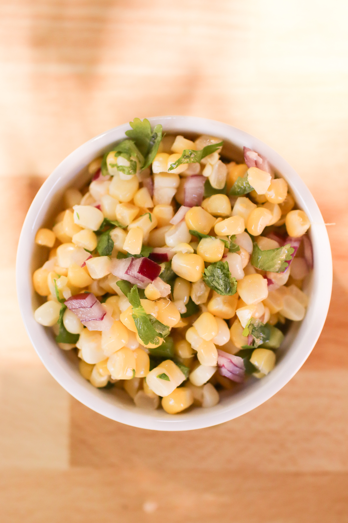 A white bowl of corn salsa on a wooden board. 