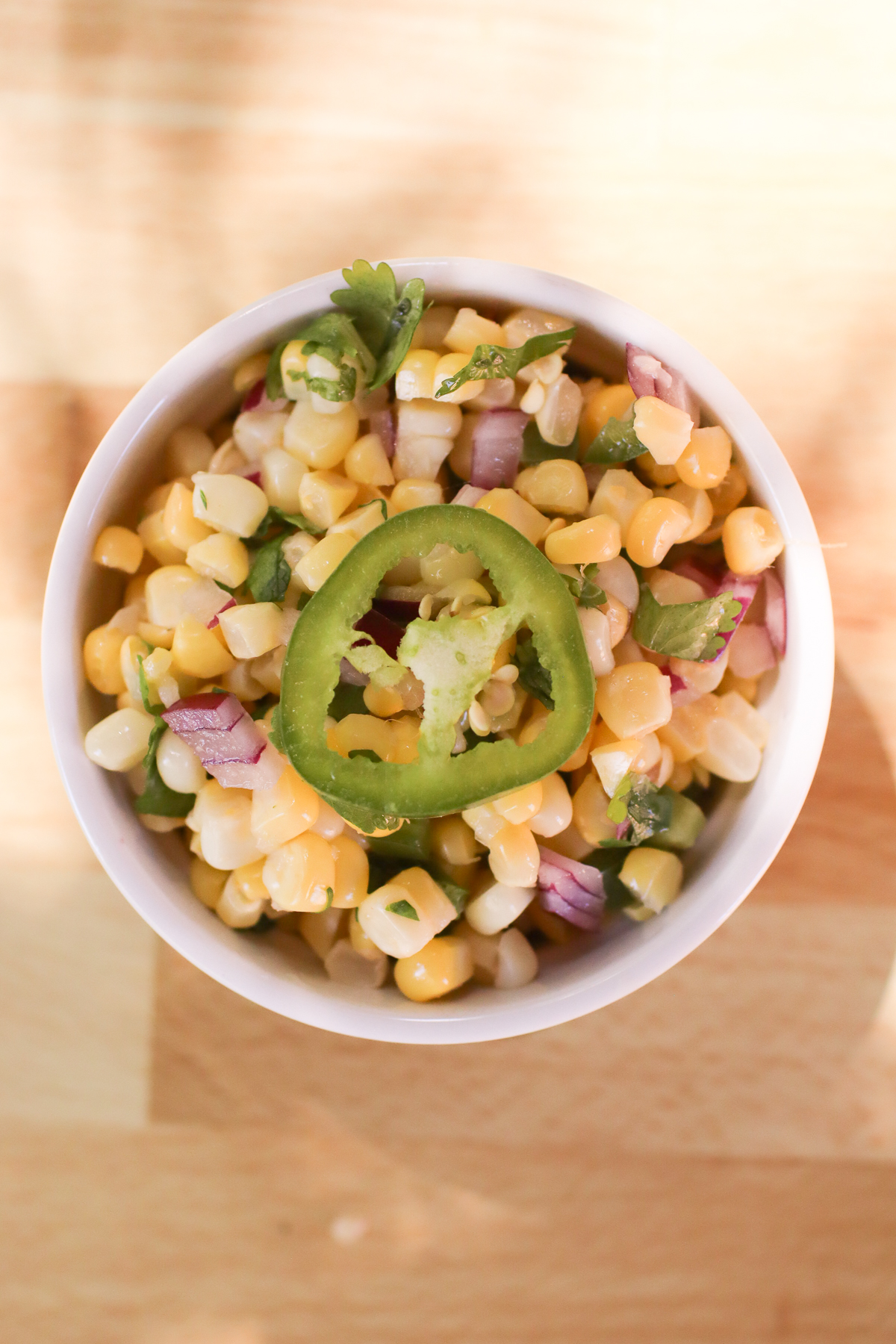 Corn salsa in a white serving bowl with a slice of jalapeno on top. 